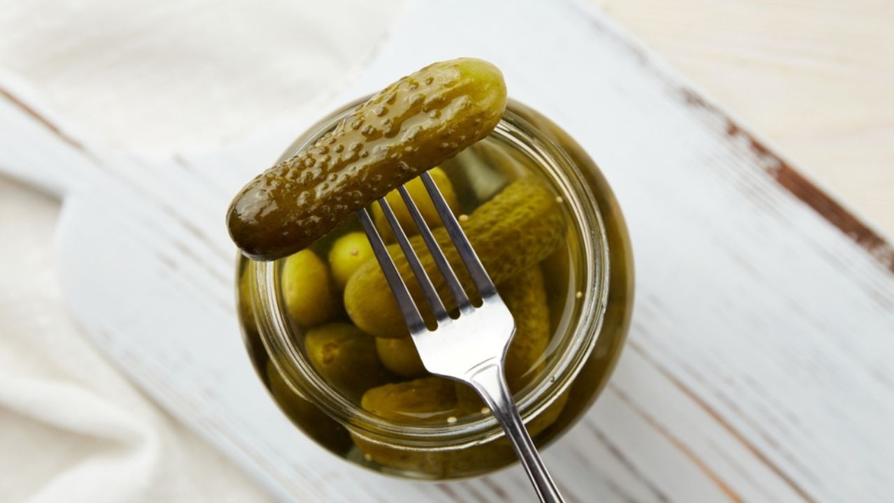 Τα αγγούρια τουρσί σε ένα πιρούνι και σε ένα βάζο σε ξύλινο φόντο.